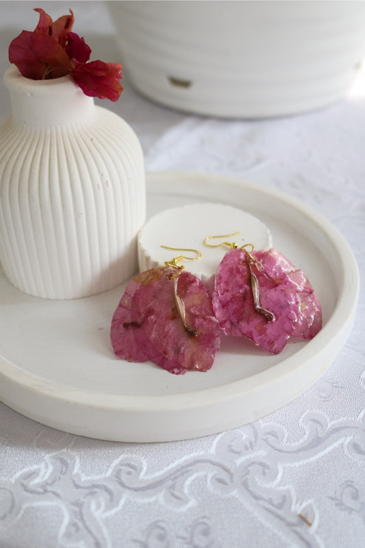 Pink earrings on a white dish with a white vase and red flower in the background.