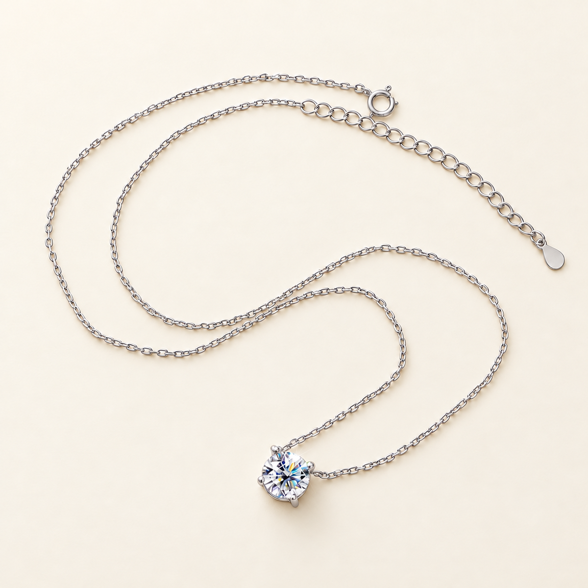 Silver solitaire necklace with extension chain and spring-ring clasp, arranged on an ivory background