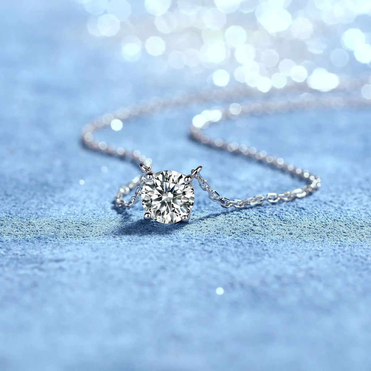 Supplier photograph of the silver four-prong solitaire necklace arranged on a blue textured background